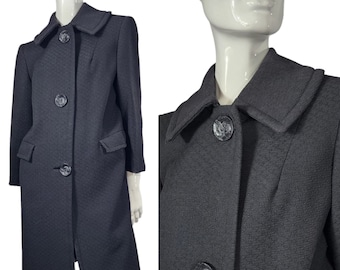 May include: A long-sleeved, black, textured coat with a large collar and four black buttons. The coat has two pockets on the front.