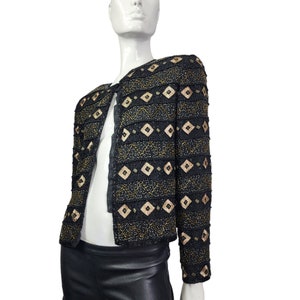 May include: A black beaded jacket with gold and brown geometric patterns. The jacket has a long sleeve and a cropped length.