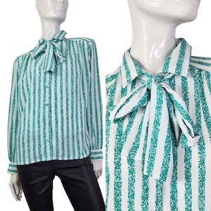 Könnte beinhalten: Eine weiße Bluse mit türkisfarbenen Streifen und einer Schleife. Die Bluse hat lange Ärmel und einen Knopfleisten vorne.