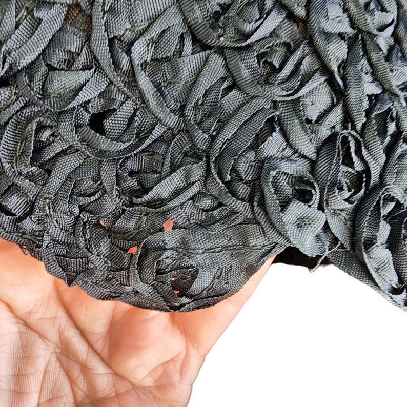 May include: Close-up of a black fabric with a textured, floral design. The fabric is made of thin, woven strips that are twisted and layered to create a three-dimensional effect.