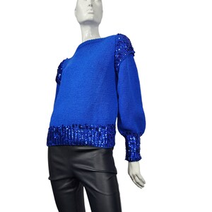 May include: A royal blue sweater with a sequined trim around the neckline, cuffs, and hem. The sweater has a relaxed fit and long sleeves.