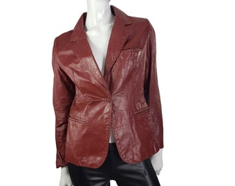 May include: A maroon blazer with a single-button closure, notched lapels, and two front pockets. The jacket is displayed on a mannequin. The blazer has a textured, leather-like appearance.