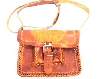 May include: A brown leather crossbody bag with a flap closure and a buckle. The bag has a front pocket and decorative stitching around the edges.