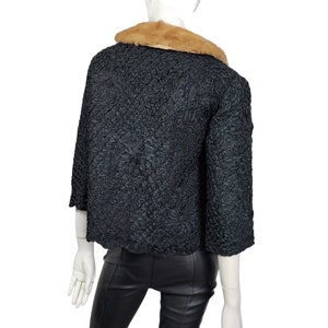 May include: A black, textured, cropped jacket with a brown fur collar. The jacket has a scalloped hem and three-quarter sleeves.