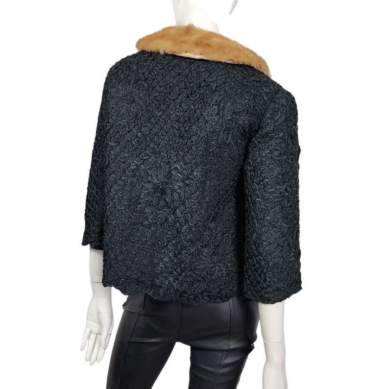 May include: A black, textured, cropped jacket with a brown fur collar. The jacket has a scalloped hem and three-quarter sleeves.