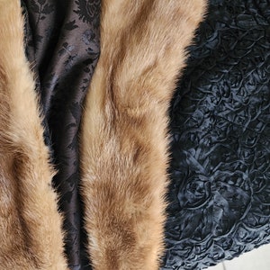 May include: A brown fur stole with a black fabric lining. The fabric has a textured, floral design.