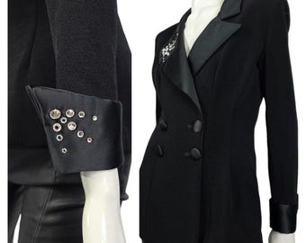 Puede incluir: Blazer negro de doble botonadura con solapas y puños de satén. Los puños están adornados con pedrería plateada. El blazer tiene un corte entallado y un diseño clásico. La prenda se exhibe en un maniquí.