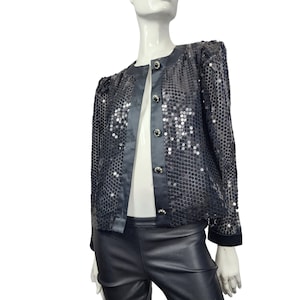 May include: A black sequin jacket with a satin trim and four decorative buttons. The jacket is displayed on a mannequin and has a round neckline and long sleeves. The jacket is paired with black leather pants.