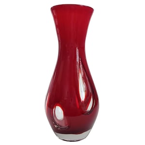 Peut inclure: Un vase en verre rouge avec un motif en verre clair. Le vase a un col étroit et une base large.