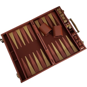 Puede incluir: Tablero de backgammon abierto en un tono marrón rojizo con triángulos dorados y marrón rojizo. Incluye dados, fichas y cubiletes de dados de cuero. El tablero tiene un asa para facilitar el transporte.