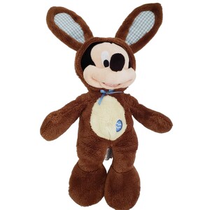 Pode incluir: Um Mickey Mouse de pel&uacute;cia castanho vestido com uma fantasia de coelho. A fantasia apresenta orelhas grandes com um padr&atilde;o xadrez azul e branco, um la&ccedil;o azul claro e uma barriga creme com um desenho de ovo de P&aacute;scoa azul. O brinquedo &eacute; para a P&aacute;scoa.