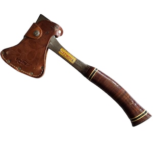 May include: A steel hatchet with a stacked leather handle featuring black and yellow rings. The blade is covered by a tan, embossed leather sheath with a metal snap button. A yellow label on the metal neck reads Estwing Made in U.S.A.