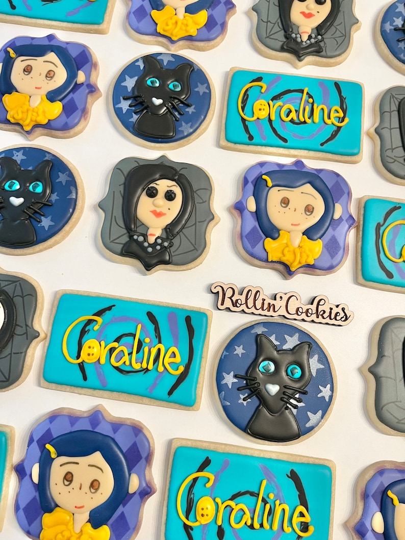 May include: A set of decorated sugar cookies featuring characters and themes from the movie Coraline. The cookies are decorated with blue, purple, yellow, black, and white icing. The cookies feature the text "Coraline" and "Rollin' Cookies".