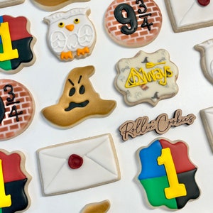 May include: A set of 12 Harry Potter themed sugar cookies decorated with various characters and symbols from the books and movies. The cookies are decorated with icing and include images of Harry Potter, Ron Weasley, Hermione Granger, Dumbledore, Snape, the Golden Snitch, the Sorting Hat, the Hogwarts Express, and the Hogwarts crest.