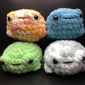 May include: Four handmade crochet plushies in various colors: yellow, blue, green, and white. Each plushie has black safety eyes and a stitched mouth, giving them a friendly appearance. The plushies are soft and textured.