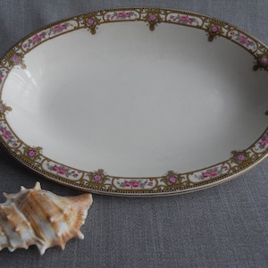 May include: An oval serving dish with a white background and a gold and pink floral border.