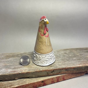 May include: A ceramic chicken figurine with a white and brown speckled body, a pink comb and wattle, and a white base with a decorative floral design.