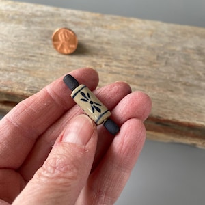 May include: A miniature ceramic rolling pin with a blue and white floral design. The rolling pin is approximately 2 inches long.