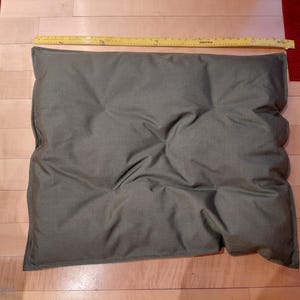 May include: A rectangular, olive-green cushion with a tufted design. A yellow ruler is placed across the top of the cushion. The cushion measures approximately 28 inches long.