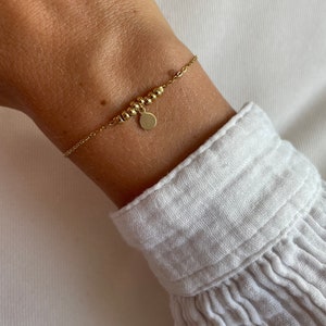 May include: A gold chain bracelet with a small round charm. The bracelet is made of small gold beads and has a delicate chain.