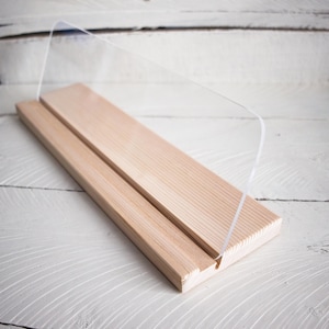 May include: A wooden display stand with a clear acrylic panel. The stand is made of light wood and has a simple design.