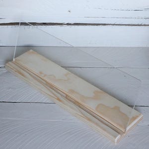 May include: A wooden shelf with a clear acrylic front. The shelf is made of natural wood with a light brown color. The shelf is perfect for displaying small items.