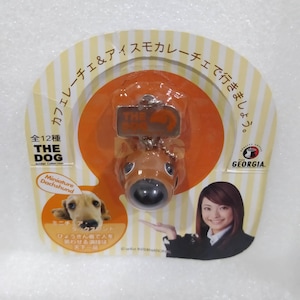 May include: A miniature Dachshund keychain in a clear plastic package. The brown dog has a large black nose and a silver tag that says "THE DOG". The packaging has Japanese text and a picture of a woman.