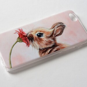Puede incluir: Una funda de tel&eacute;fono blanca con una imagen pintada de un conejo marr&oacute;n oliendo una flor roja.
