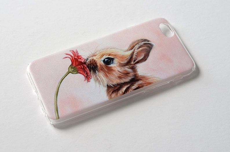 Puede incluir: Una funda de tel&eacute;fono blanca con una imagen pintada de un conejo marr&oacute;n oliendo una flor roja.