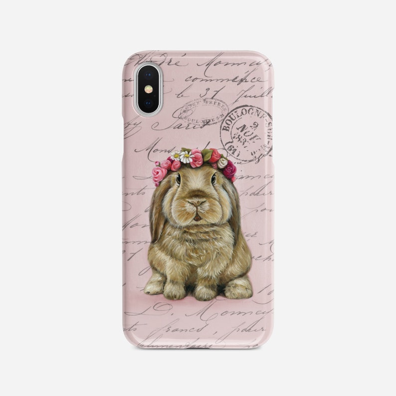 May include: A phone case featuring a brown bunny wearing a floral crown, set against a pink background with script and stamps. The case has a glossy finish and a camera cutout.