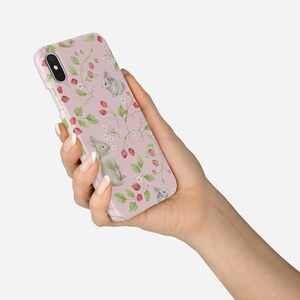 May include: A pink phone case with a pattern of white rabbits, green leaves, and red strawberries.