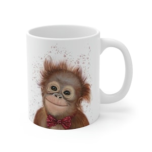 May include: White ceramic mug with a watercolor illustration of a smiling orangutan wearing a red bow tie. The background is a white splatter pattern.