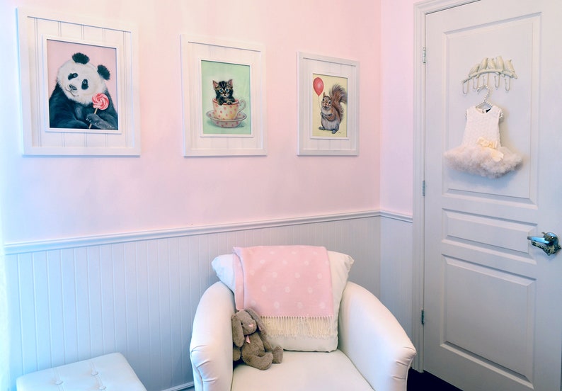 Puede incluir: Una habitaci&oacute;n de beb&eacute; rosa y blanca con un sill&oacute;n blanco, una manta rosa y blanca y un conejito de peluche. Hay tres cuadros enmarcados en la pared con im&aacute;genes de un panda, un gatito y una ardilla.