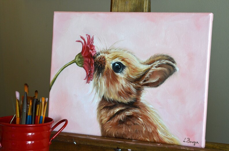 Puede incluir: Una pintura de un conejo marr&oacute;n oliendo una flor roja sobre un fondo rosa. El conejo tiene un ojo negro y un pelaje marr&oacute;n y esponjoso. La pintura est&aacute; firmada "L. Bergen" en la esquina inferior derecha.