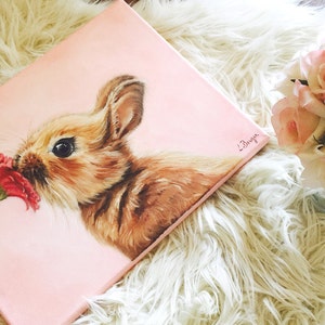May include: A painting of a brown bunny rabbit sniffing a red flower on a pink background. The painting is signed "L.Bryon".