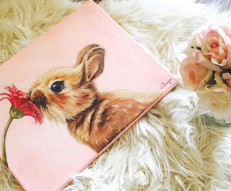 May include: A painting of a brown bunny rabbit sniffing a red flower on a pink background. The painting is signed "L.Bryon".