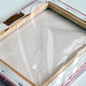 May include: A wrapped canvas painting with a wooden frame and a pink backing. The canvas is wrapped around the frame and secured with staples. The painting is protected by a clear plastic wrap.