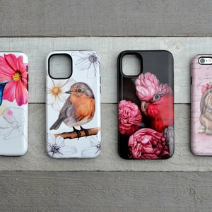 May include: Four phone cases with nature-themed designs. One case features a hummingbird and pink flower, another a robin on a branch, a third a pink cockatoo with flowers, and the last a bunny with a floral crown.