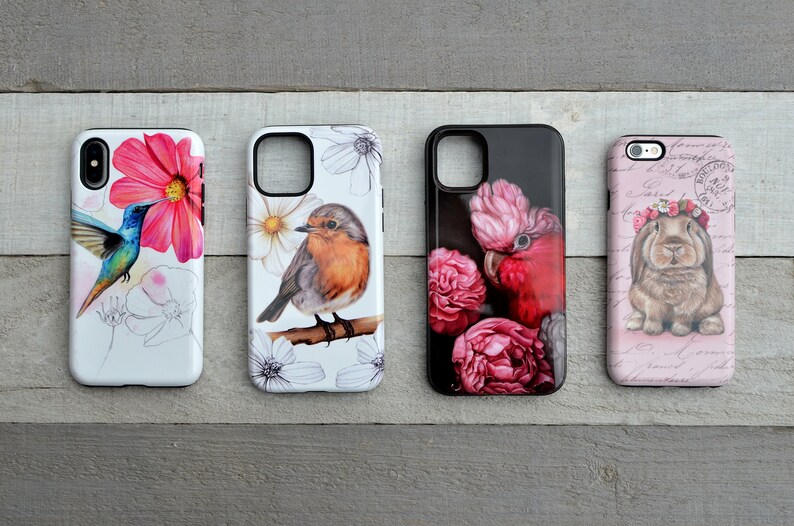 May include: Four phone cases with nature-themed designs. One case features a hummingbird and pink flower, another a robin on a branch, a third a pink cockatoo with flowers, and the last a bunny with a floral crown.
