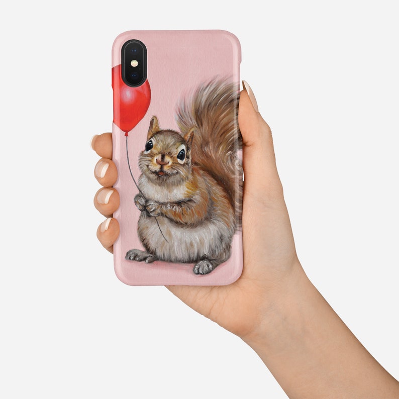 May include: A pink phone case with a cute squirrel holding a red balloon. The squirrel is brown and gray with a bushy tail.
