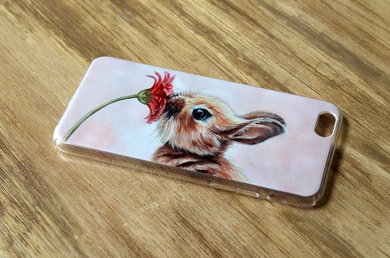 Puede incluir: Una funda de tel&eacute;fono transparente con un dise&ntilde;o pintado de un conejo marr&oacute;n oliendo una flor roja.