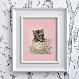 Puede incluir: Un lindo gatito tabby con ojos azules se sienta dentro de una taza de t&eacute; rosa con lunares blancos. La taza de t&eacute; est&aacute; sobre un platillo a juego. La imagen est&aacute; sobre un fondo rosa.