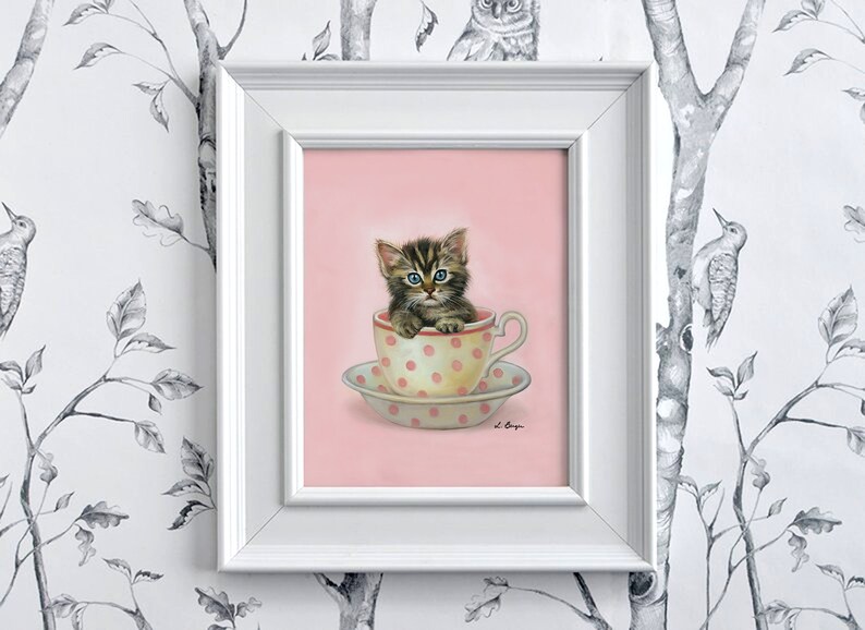 Puede incluir: Un lindo gatito tabby con ojos azules se sienta dentro de una taza de t&eacute; rosa con lunares blancos. La taza de t&eacute; est&aacute; sobre un platillo a juego. La imagen est&aacute; sobre un fondo rosa.