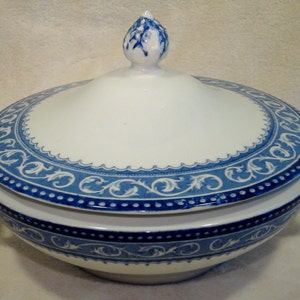 May include: White and blue ceramic soup tureen with a lid. The tureen features a blue decorative border with a floral design and handles on each side. The lid has a decorative finial.