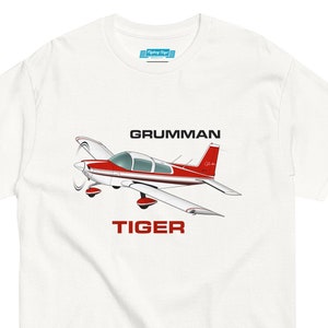 May include: White t-shirt with a red and white cartoon illustration of a Grumman Tiger airplane. The text "GRUMMAN" and "TIGER" are printed in black below the airplane.
