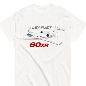 May include: White t-shirt with a graphic of a Learjet 60XR private jet. The text "LEARJET 60XR" is printed in red on the shirt.