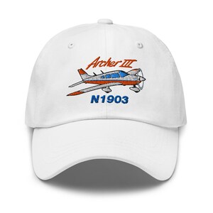 May include: White baseball cap with an embroidered design of a red, orange, and blue airplane, the text "Archer III" and "N1903". The cap has a curved peak and a classic six-panel design.