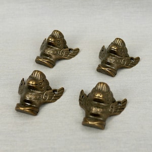 May include: Four gold-toned metal furniture feet shaped like a mythical creature with wings. The feet are detailed with intricate designs.