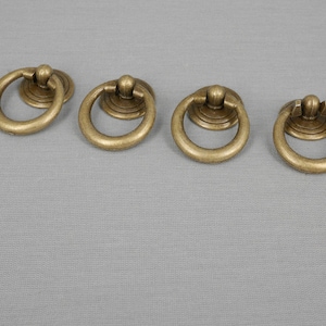 May include: Four antique gold-toned ring pulls with a decorative knob on top. The ring pulls are all the same size and shape.