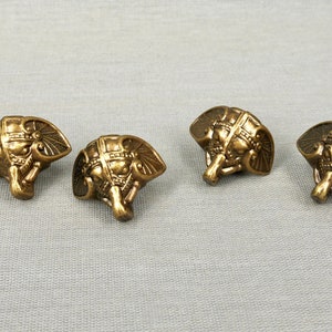 May include: Four gold-colored metal elephant head-shaped decorative embellishments.